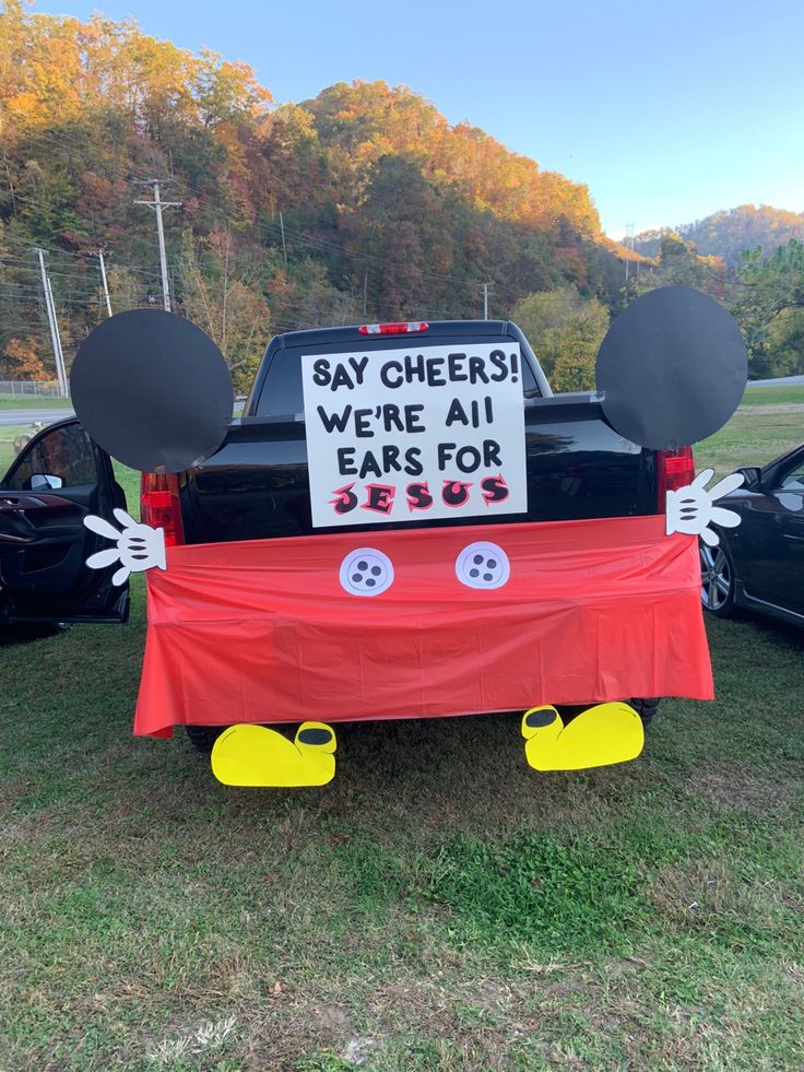 a mickey mouse car is parked in the grass with a sign that says say cheers we're all ears for