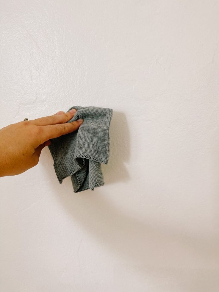 a hand holding a cloth on top of a white wall