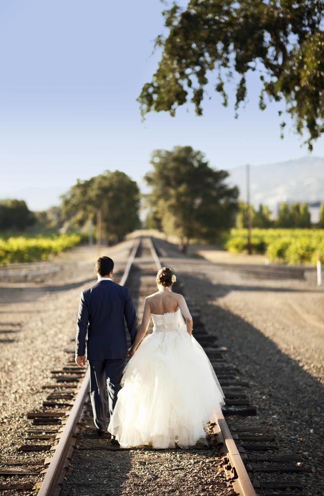 the bride and groom are walking down the railroad tracks holding each other's hands