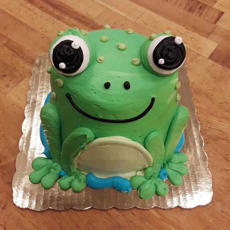 a green frog cake with googly eyes sitting on top of a silver plate covered in foil