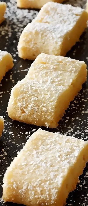 several pieces of cake sitting on top of a black pan covered in powdered sugar