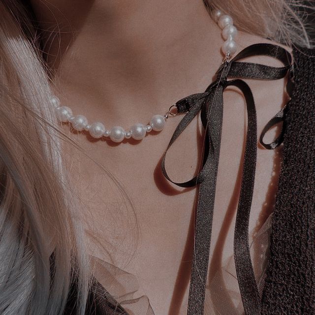 a close up of a woman wearing a necklace with pearls and black ribbon on it