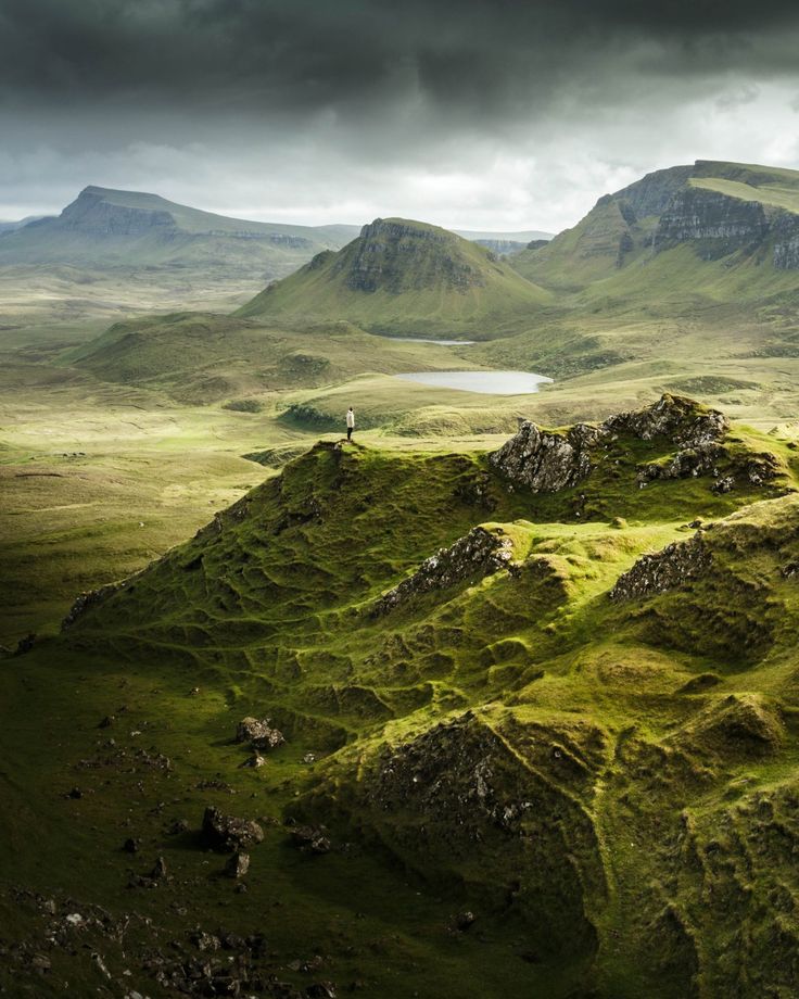 a man standing on top of a lush green hill next to a body of water