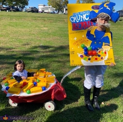 two children in costumes standing next to a wagon with gummy bears on it