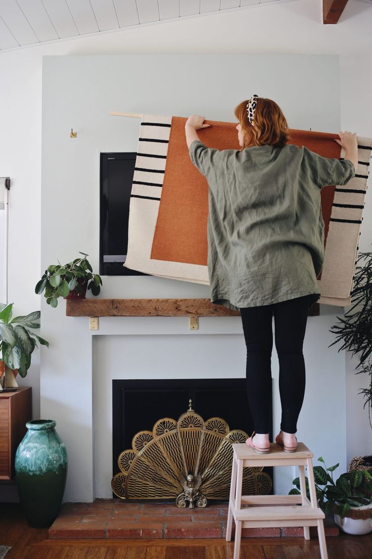 a woman standing on a stool in front of a fire place holding up a rug