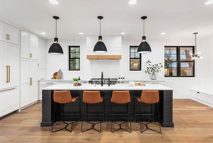 a large kitchen with an island and bar stools next to it, along with three lights hanging from the ceiling