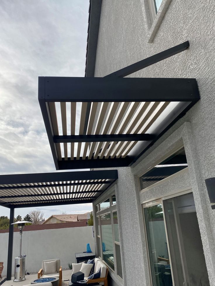 an outdoor living area with patio furniture and pergolated roofing on the side of a house