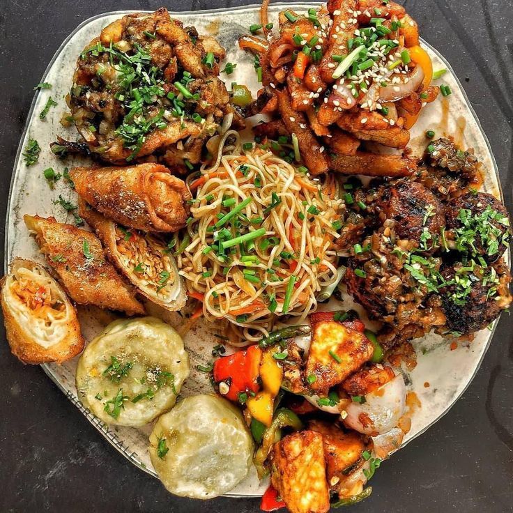 a plate full of food with meat, noodles and veggies on the side