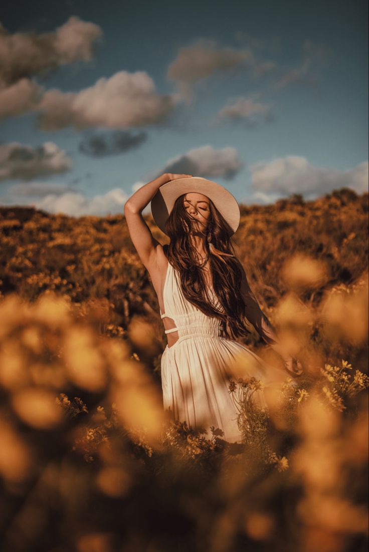 a woman wearing a white dress and hat standing in the middle of a field with yellow flowers