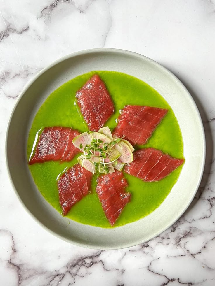 a white plate topped with slices of fish on top of green sauce and garnish