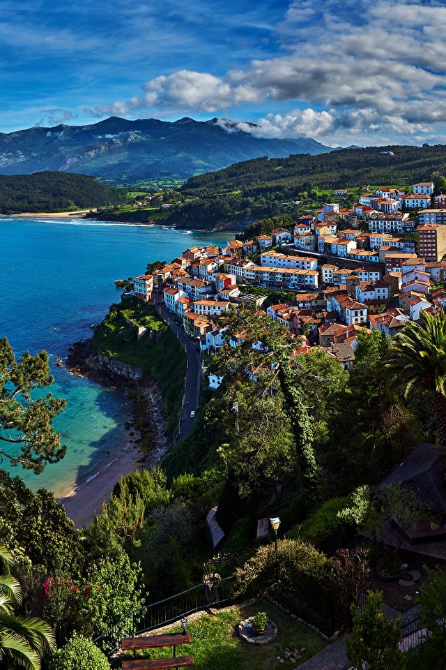 an aerial view of a town on the coast with mountains in the background and blue water