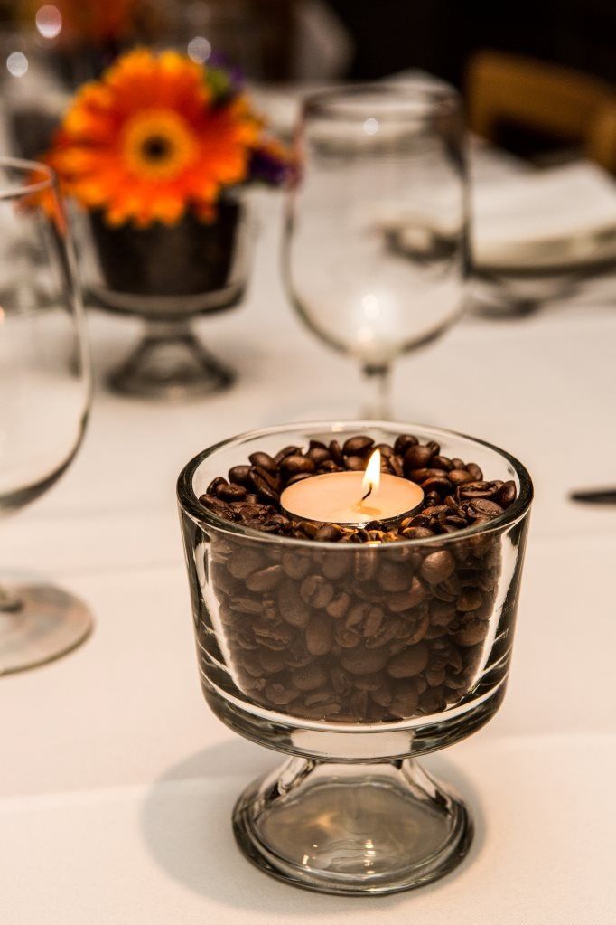 a glass bowl filled with coffee beans sitting on top of a white table covered in wine glasses