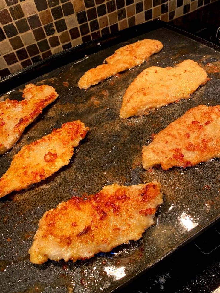 several pieces of chicken sitting on top of an oven pan in the process of being cooked