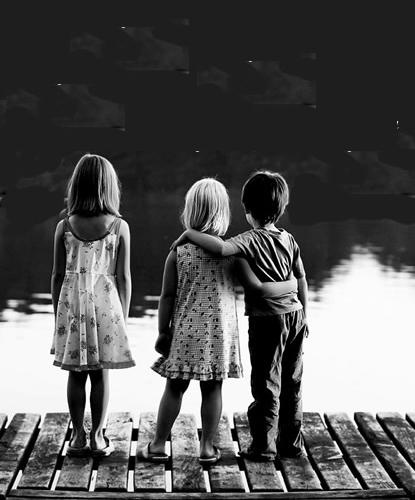 three children standing on a dock looking at the water