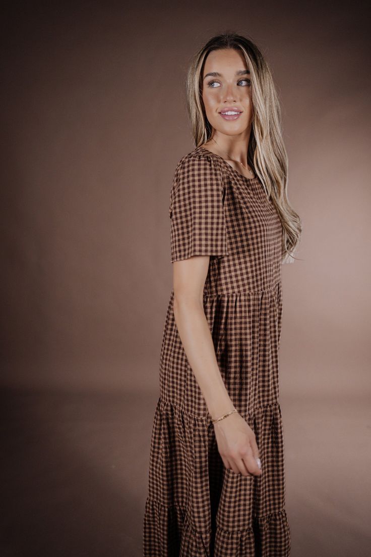 Indulge in the sophistication of the Taryn Gingham Dress on Brown. Made from 100% cotton, this midi dress boasts a modest silhouette and timeless gingham print, making it the perfect fall dress. Elevate your wardrobe with this premium piece that exudes elegance and style. 100 Cotton Model Measurements: Hips 36” Waist 25” Bust: 31”, Height 5’5.5, wearing a size small Plaid Midi Dress With Ruffles For Picnic, Picnic Plaid Midi Dress With Ruffles, Knee-length Ruffled Midi Dress For Picnic, Plaid Ruffled Midi Length Dress, Plaid Ruffled Midi Dress, Gingham Plaid Knee-length Dress With Ruffles, Ruffled Midi Plaid Dress, Plaid Midi Dress With Ruffles, Brown Cotton Midi Dress For Daywear