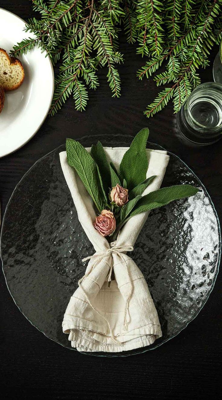 a black plate topped with a napkin covered in flowers and greenery next to two slices of bread