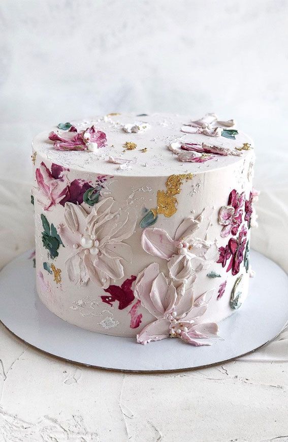 a white cake with pink and yellow flowers on it sitting on a plate in front of a white background