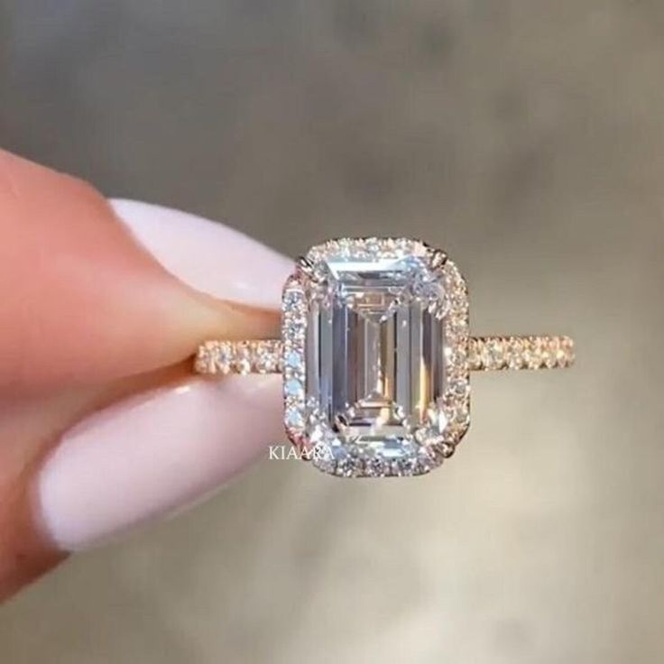 a close up of a person's hand holding a ring with an emerald stone