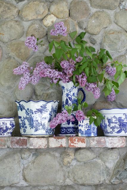 purple flowers are in blue and white vases on a stone ledge next to a brick wall