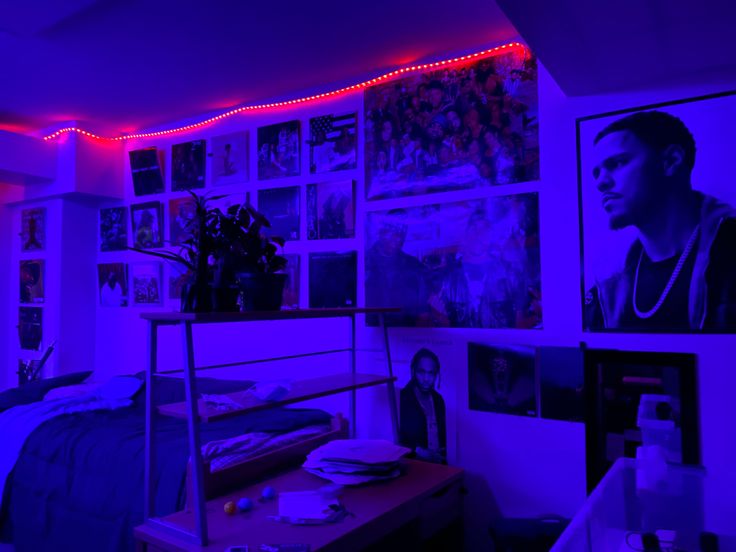 a room with purple lighting and pictures on the wall, including a bed in front of a desk