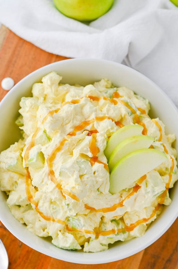 a white bowl filled with mashed potatoes and sliced apples on top of a wooden cutting board