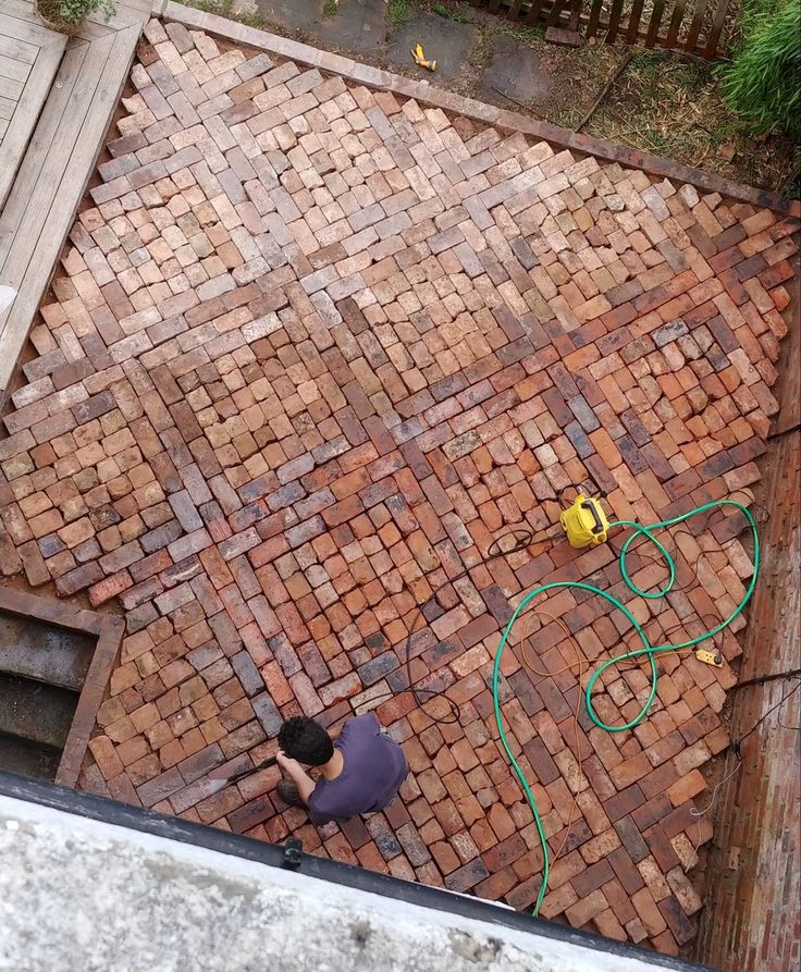 an overhead view of a man working on a brick patio with a hose attached to it