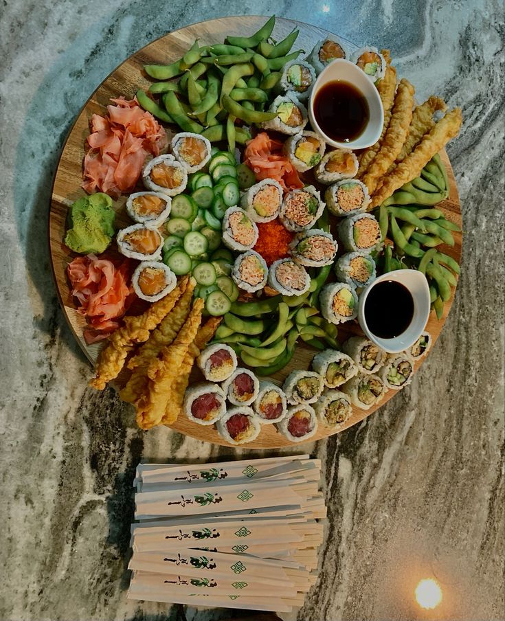 an assortment of sushi on a wooden platter with chopsticks and dipping sauce