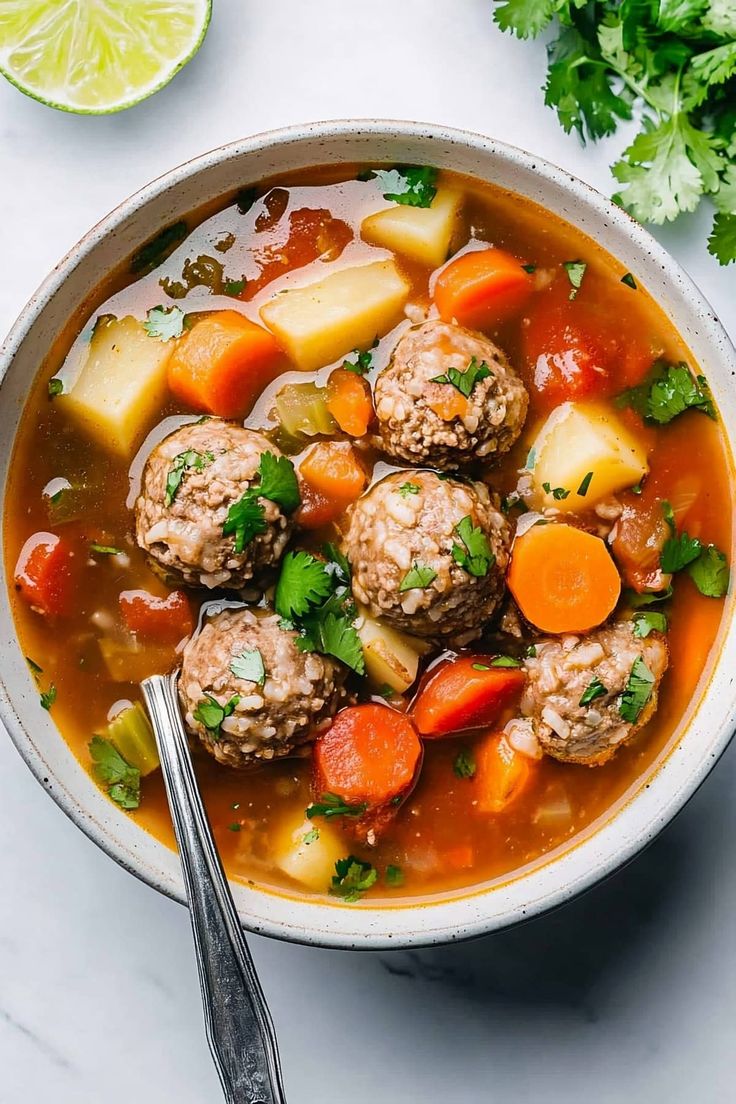 a bowl filled with meatballs and vegetables next to a lime wedge on the side