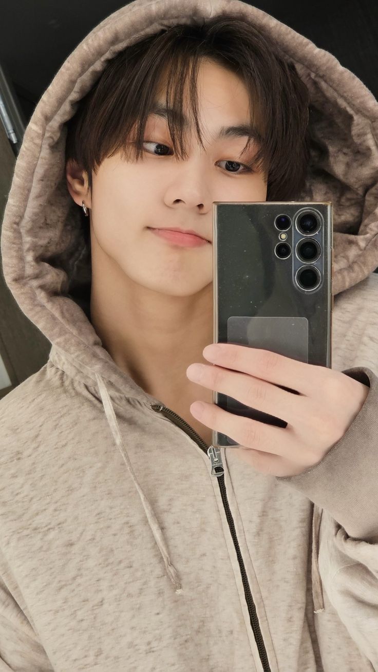 a young man taking a selfie with his cell phone in front of him and wearing a hoodie