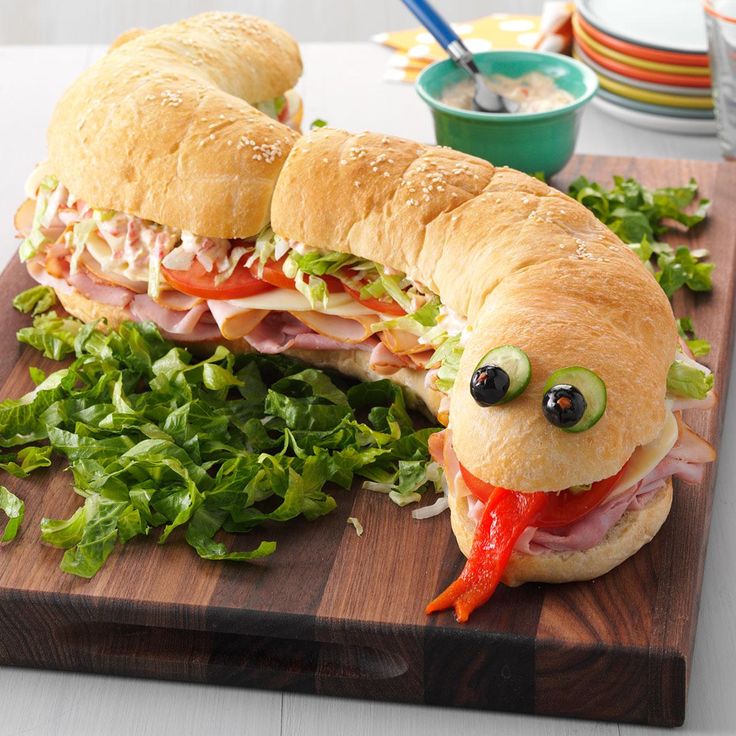 two sandwiches on a cutting board with lettuce, tomato and other food items