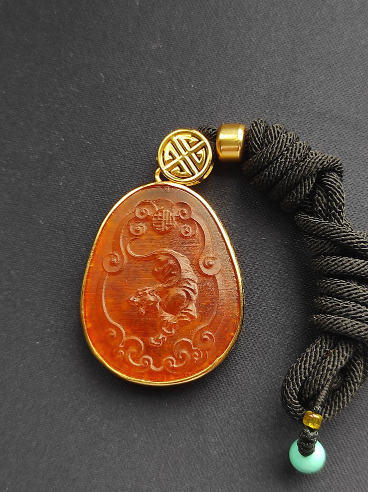 Natural Amber Hand carved Amber  Pendant Necklace Natural amber pendant with hand woven rope necklace 1.Material : A thin layer of gold plated sterling silver 2.Color:  Honey colored amber 3.Gemstone: Amber 4.This is a traditional Chinese style pendant. The pendant has the Chinese zodiac tiger carved on it surrounded by auspicious clouds. The back of the pendant is uneven but sparkles lively. 5.Size: 36mm*29mm Note: No Return Allowed.            We will send a Certified mail. Chinese Zodiac Tiger, Amber Pendant, Natural Amber, Honey Colour, Chinese Zodiac, Rope Necklace, Oval Pendant, Traditional Chinese, Gold Plated Sterling Silver