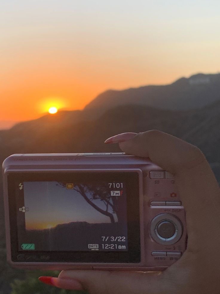 a person holding up a camera with the sun setting in the background