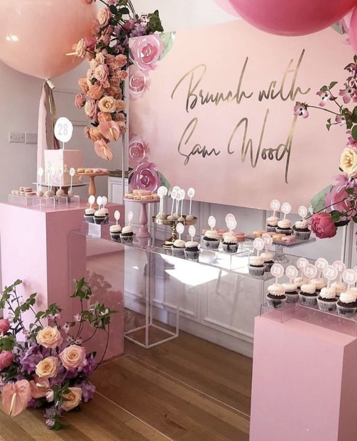 a table with cupcakes and flowers on it in front of a pink sign