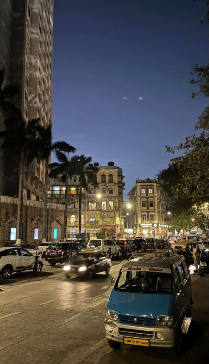 cars driving down the street at night in an urban area with tall buildings and palm trees