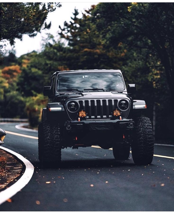 a jeep driving down the road with trees in the background and leaves on the ground