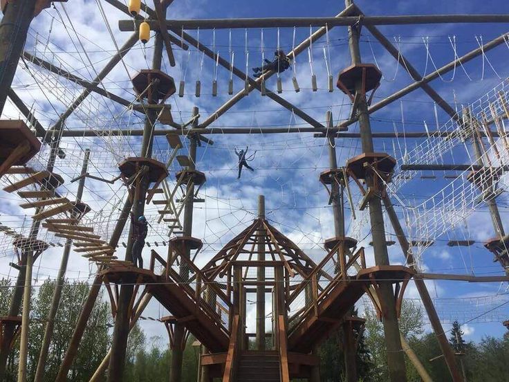 an overhead view of a wooden structure with ropes and ladders on the sides, against a blue cloudy sky