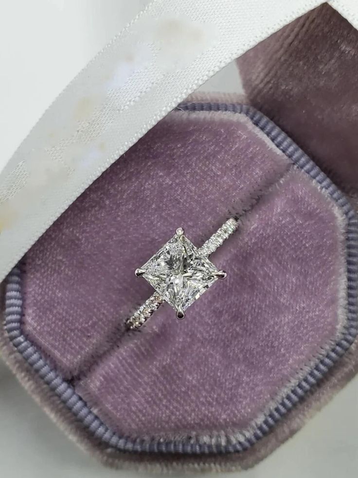 an engagement ring with a princess cut diamond set in white gold on top of purple velvet