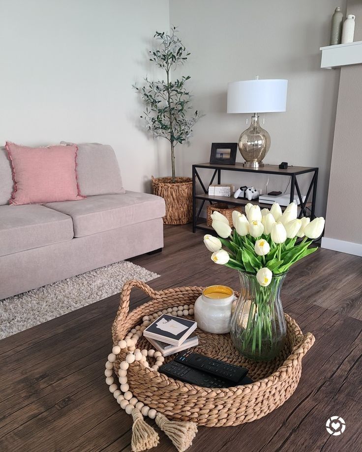 a living room with a couch, coffee table and flowers in a vase on the floor