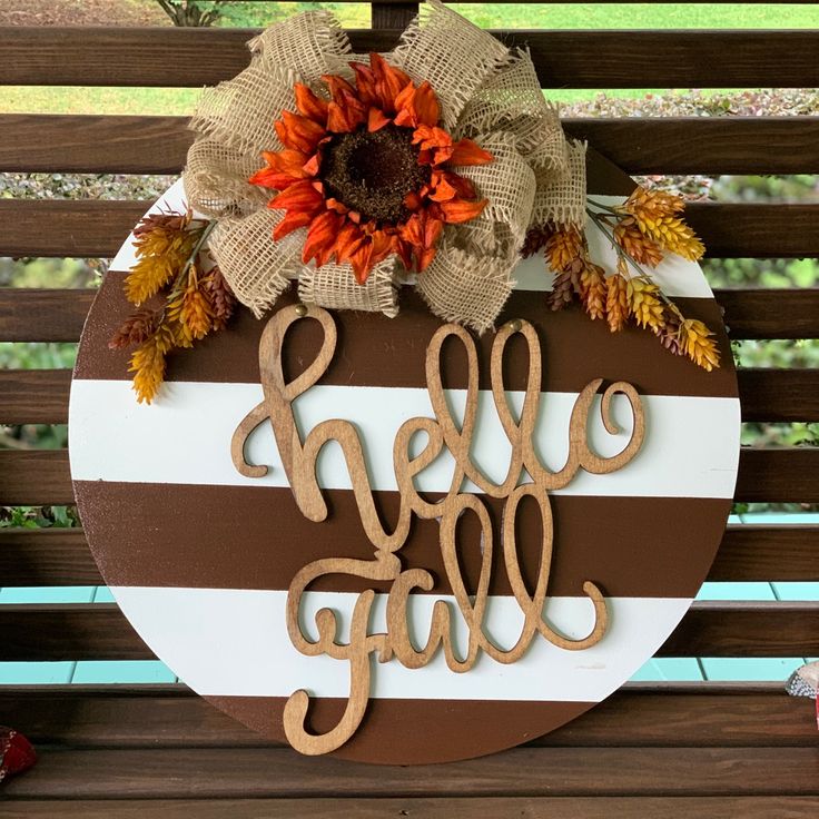 a wooden sign that says hello fall on the side of a bench with autumn decorations