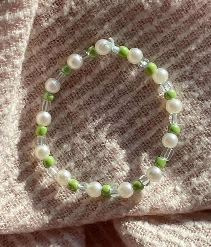 a green and white beaded bracelet sitting on top of a blanket