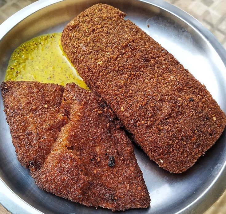 two fish fillets in a metal bowl with yellow sauce on the side and another piece of bread