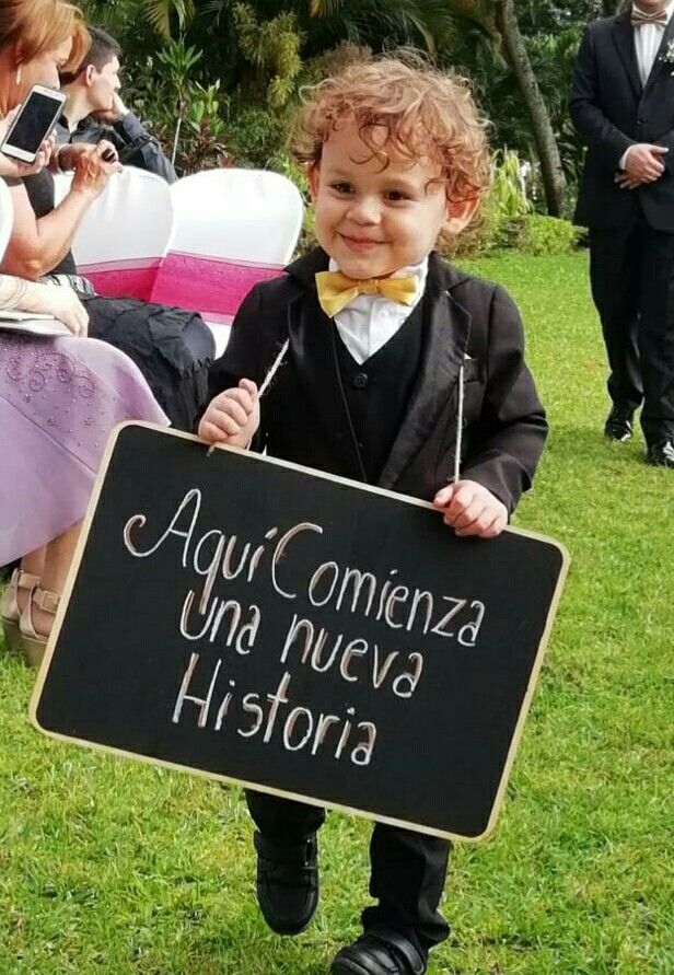 a little boy dressed in tuxedo and bow tie holding a sign that says agui comenza una nueved historia