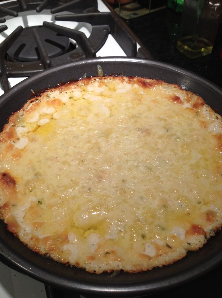 a cheese pizza sitting on top of a stove next to a frying pan filled with food