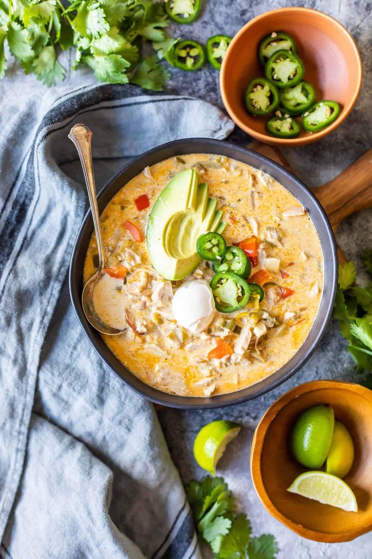 two bowls filled with soup next to limes and avocado on a table