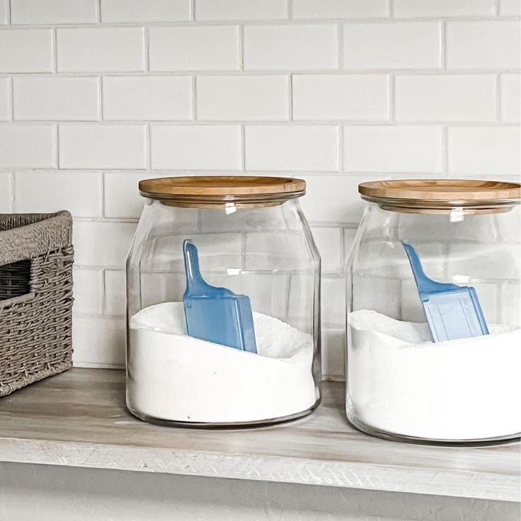 two glass jars with toothbrushes in them sitting on a shelf next to a basket