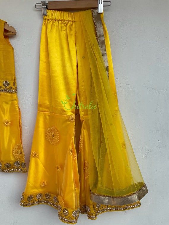 Goergeous yellow suit is suitable for mehandi/ Haldi functions.The outfit consist of top, flared pant and scarf.Silk, satin, tulle and cotton used to make this outfit.The dress is fully lined with cotton.Pant waist is elasticated.Size: All sizes possible.Price listed for baby girls age 4-8 years. Yellow Chanderi Palazzo Set With Sheer Dupatta, Bollywood Style Yellow Raw Silk Palazzo Set, Yellow Palazzo Set With Sheer Dupatta For Wedding, Wedding Palazzo Set In Yellow Chanderi, Wedding Yellow Chanderi Palazzo Set, Diwali Yellow Palazzo Set With Dupatta, Wedding Chanderi Pant Set With Gota Work, Yellow Palazzo Set With Dupatta For Diwali, Yellow Chanderi Palazzo Set For Wedding