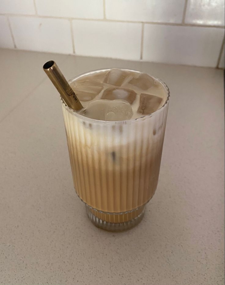 a drink in a glass with ice and a gold straw sticking out of the top