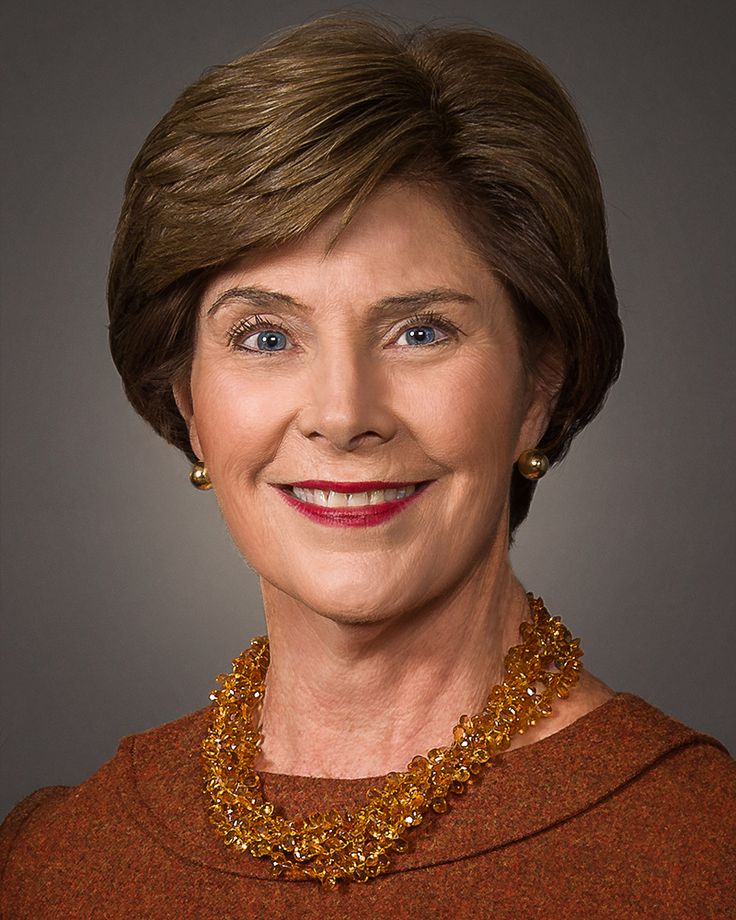 a woman wearing a brown sweater and gold necklace smiling at the camera with her eyes wide open