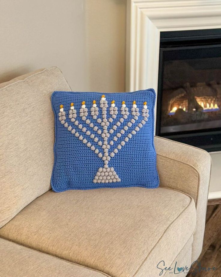 a crocheted menorah pillow sitting on a couch in front of a fireplace