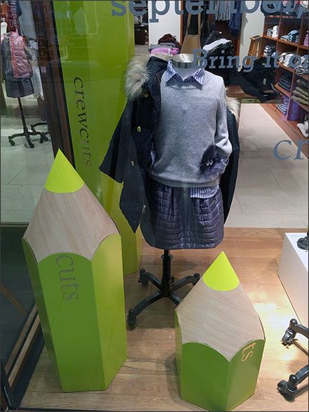 a mannequin in a store window with green paper cones and clothes on display